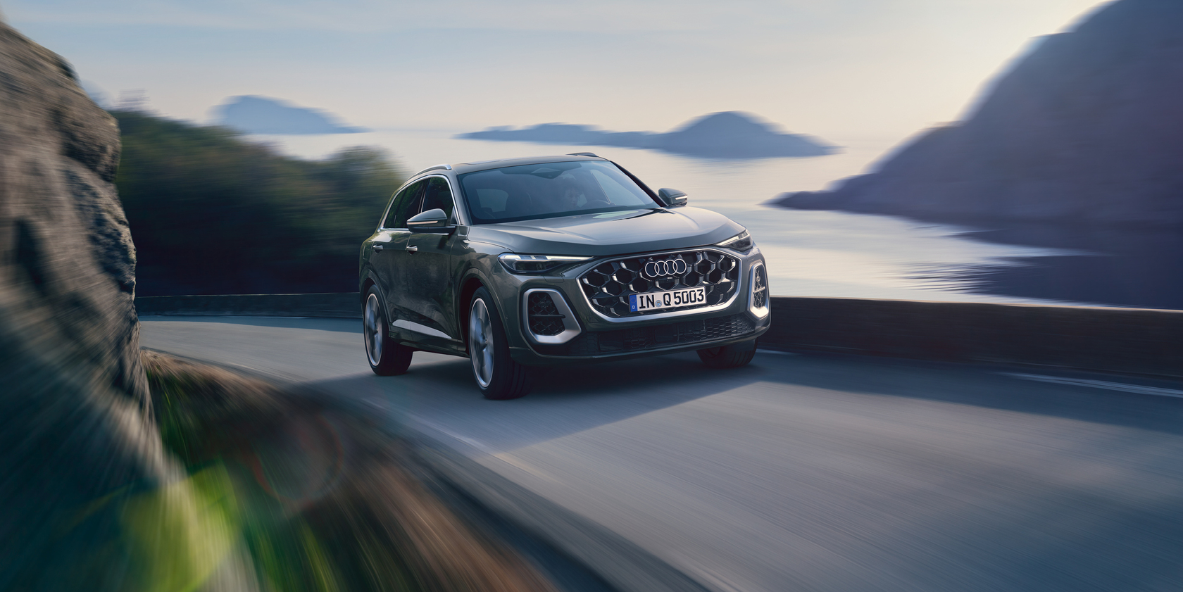 Ein Audi Q5 SUV fahrend auf einer Küstenstraße; im Hintergrund das Meer 