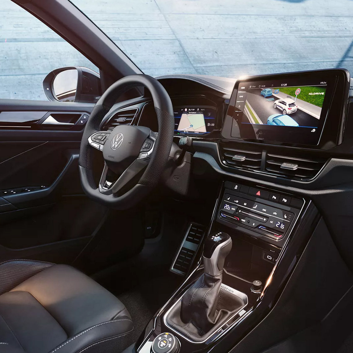 Innenansicht eines VW-Cockpits mit Lederlenkrad, großem Touchscreen mit Assistenzanzeige (iQ.DRIVE), digitalem Cockpit mit Navigationsanzeige und moderner Mittelkonsole mit Automatik Schaltknauf und Klimabedieneinheit.