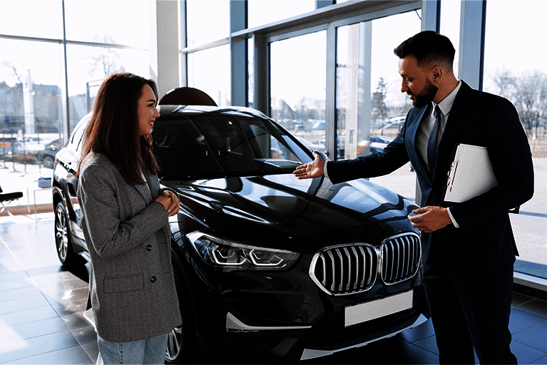 Autoverkäufer im Anzug präsentiert einer Kundin einen schwarzen BMW-SUV im Autohaus