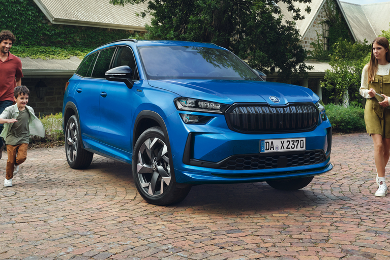 Blauer Skoda Kodiaq geparkt vor einem großen Haus, eine dreiköpfige Familie läuft um das Autos herum