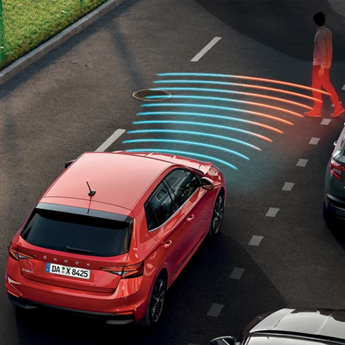 Ein roter Škoda Fabia fährt auf einer mehrspurigen Straße. Vor dem Fahrzeug erkennt man die Darstellung des Front-Assistenzsystems: blaue und rote Linien symbolisieren den aktiven Radarsensor, der einen Fußgänger vor dem Auto erkennt.
