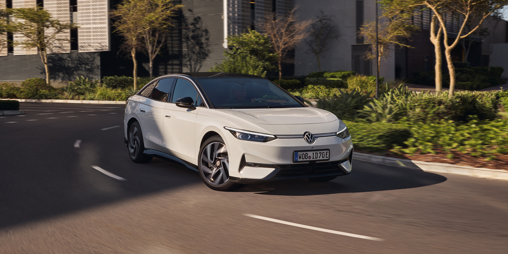 Weißer Volkswagen ID.7 fährt durch eine moderne städtische Umgebung mit viel Grün.