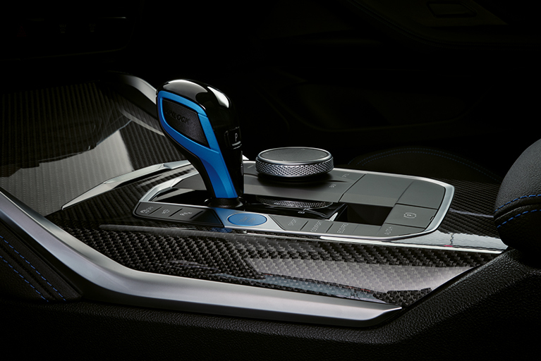 Nahaufnahme des Schalthebels eines BMW i4 M50. Der Gangschalter ist mit mattblauen Applikationen versehen, die Mittelkonsole ist in Carbon-Optik.