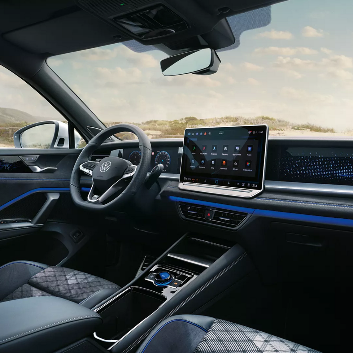Innenraum eines VW Tayron mit großem Touchdisplay und Infotainmentsystem, Multifunktionslenkrad und grau/schwarzen Sitzen mit blauen Nähten