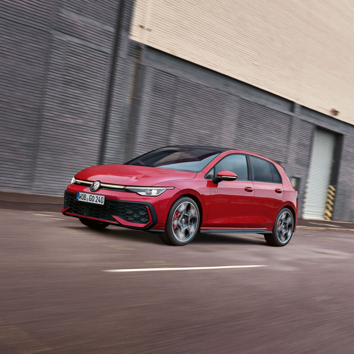 Roter VW Golf GTI in Front- und Seitenansicht fahrend auf einer städtischen Straße vor einer hohen Gebäudefassade