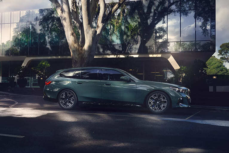 Mintfarbener BMW i5 Touring parkend an einer Straße vor einem Baum