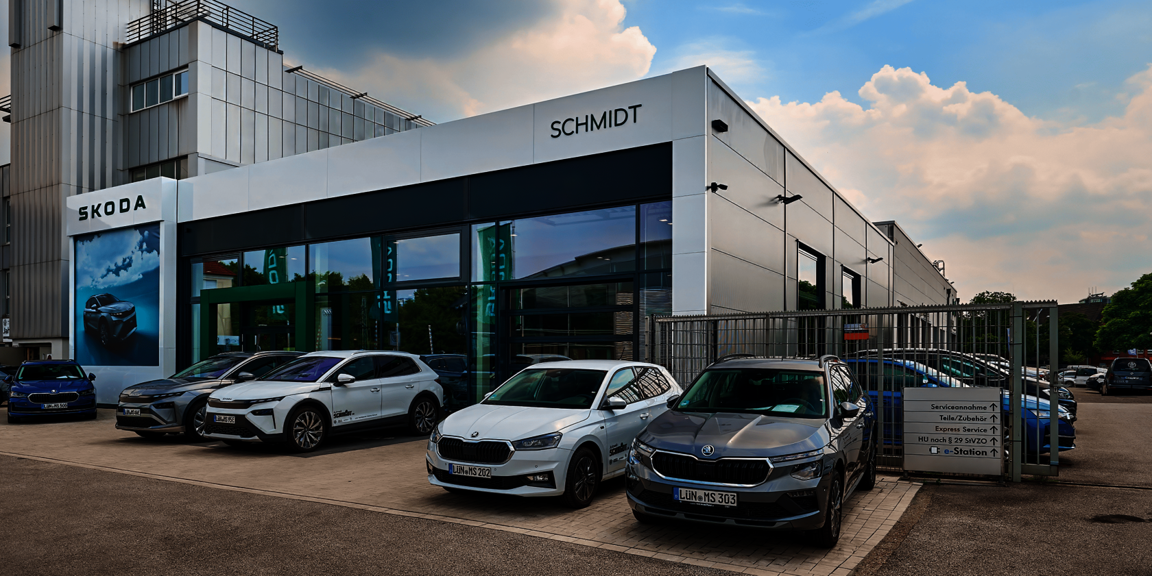 ußenansicht des ŠKODA Autohauses Schmidt in Lünen mit mehreren geparkten ŠKODA Fahrzeugen vor dem Gebäude und sichtbarem Eingang zum Haus.
