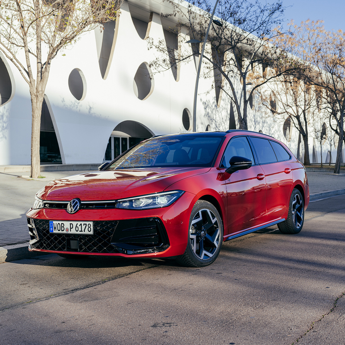 Roter VW Passat in Front- und Seitenansicht geparkt am Straßenrand vor einem modernen, weißen Gebäude