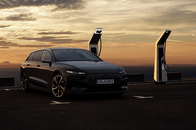 Frontansicht eines grauen Audi A6 e-tron, geparkt an einer Schnellladesäule bei Sonnenuntergang