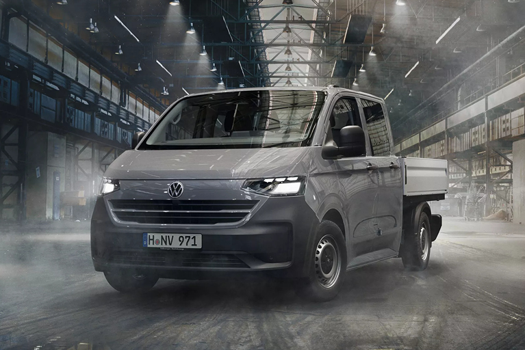 Grauer VW e-Transporter Pritschenwagen steht mittig schräg nach links zeigend, in einer Lagerhalle.