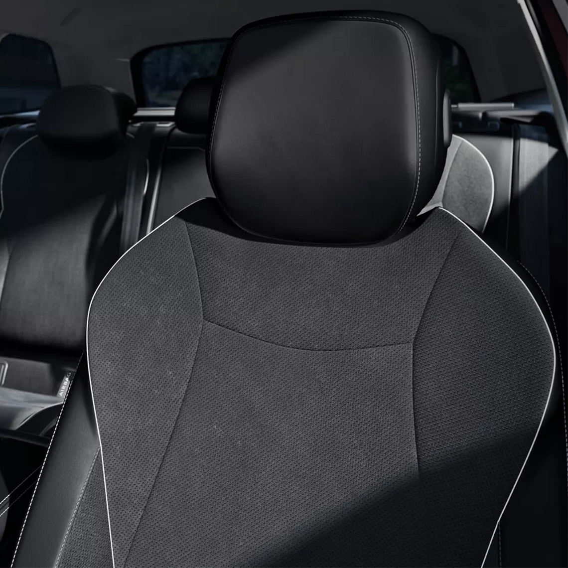 Nahaufnahme eines VW Passat-Autositzes. Die Rückenlehne ist dunkelgrau mit weißen Nähten, die Kopfstütze ist in schwarzer Lederoptik.