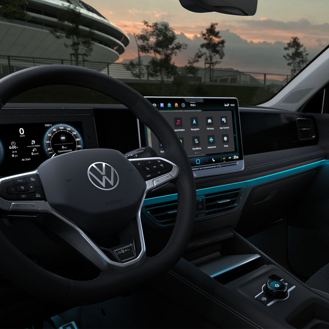 Cockpit eines VW Tiguan mit Multifunktionslenkrad, Touchdisplay mit Infotainmentsystem und blauer Ambientebeleuchtung, durch die Frontscheibe sieht man einen bewölkten Himmel bei Sonnenuntergang.