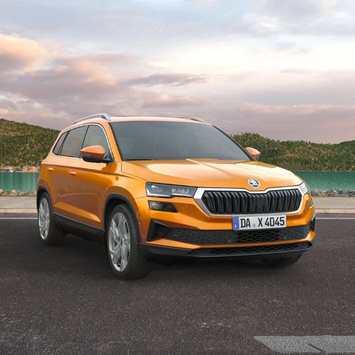 Orangefarbener Škoda Karoq in seitlicher Frontansicht steht vor einem See, im Hintergrund bewaldete Hügellandschaft