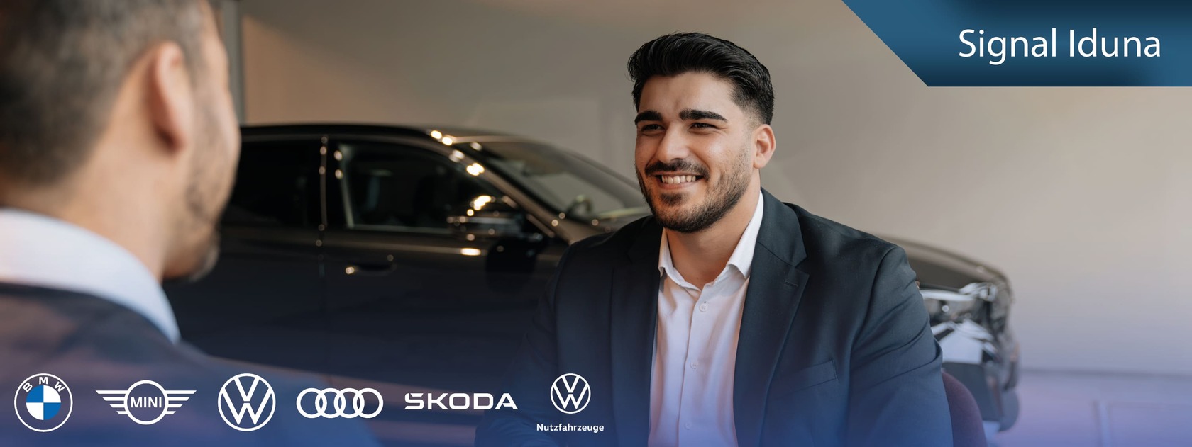 Ein Autoverkäufer im Gespräch mit einem Kunden, beide elegant gekleidet. Im Hintergrund ein schwarzes Fahrzeug im Showroom. Oben rechts befindet sich ein blaues Banner mit der Aufschrift „Signal Iduna“. Darunter sind die Markenlogos von BMW, MINI, Volkswagen, Audi, Škoda und Volkswagen Nutzfahrzeuge zu sehen.