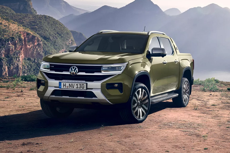 Grüner Volkswagen Amarok steht auf einem unbefestigten Untergrund vor einer weitläufigen Berglandschaft.