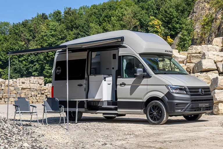 VW Grand California DUNE Camper mit Markise, geöffneten Türen und Campingmöbeln – bereit für das Abenteuer.