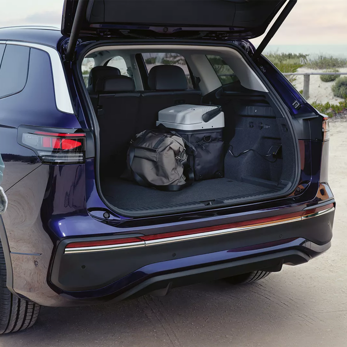 Geöffneter Kofferraum eines dunkelblauen VW Tiguan. Im Kofferraum stehen ein Rucksack sowie eine Kühltasche, welche an die Strombüchse im Kofferraum angeschlossen ist.