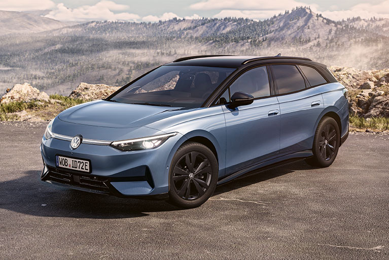 Hellblauer Volkswagen ID.7 Tourer Elektro-Kombi, schräg von vorn auf einer Bergstraße vor weiter Landschaft.