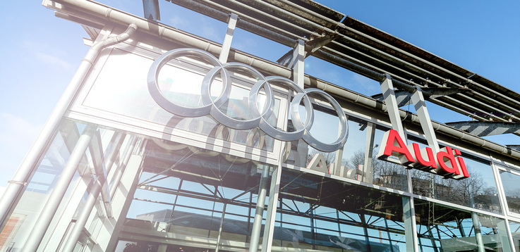 Nahaufnahme der Außenansicht des Audi-Gebäudes der Autowelt Schmidt am Standort Lünen. An der Glasfront das Audi Logo sowie ein Schild mit der Aufschrift "Audi"