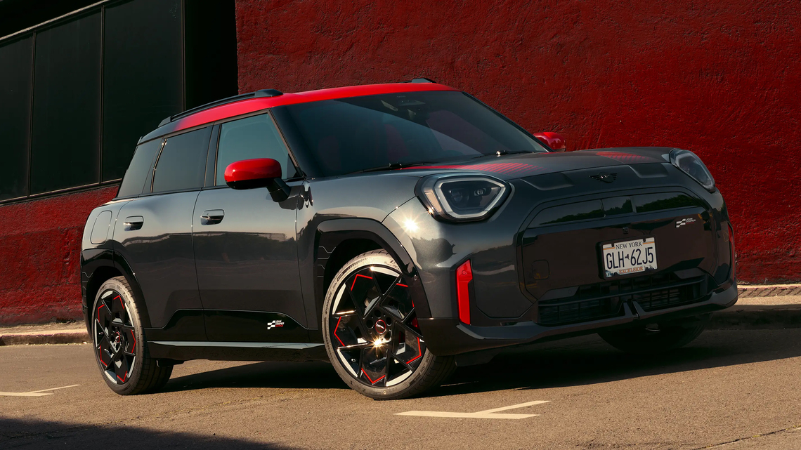 Schwarzer MINI John Cooper Works in Seiten- und Frontansicht mit roten Folierungen und Akzenten, geparkt vor einem roten Gebäude.