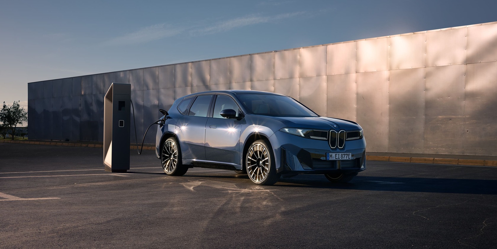 Der neue iX3 vor einem Gebäude an einer BMW Ladesäule