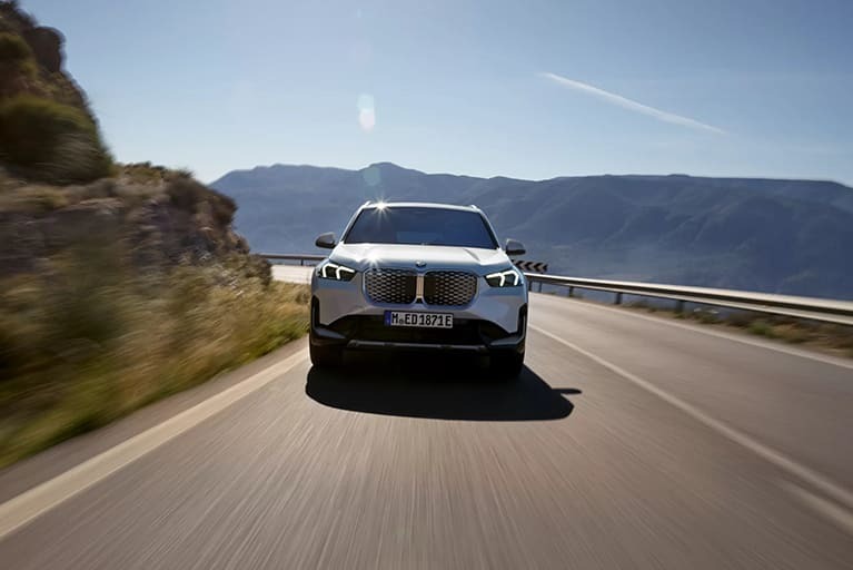 Weißer BMW iX1 fahrend auf einer Landstraße