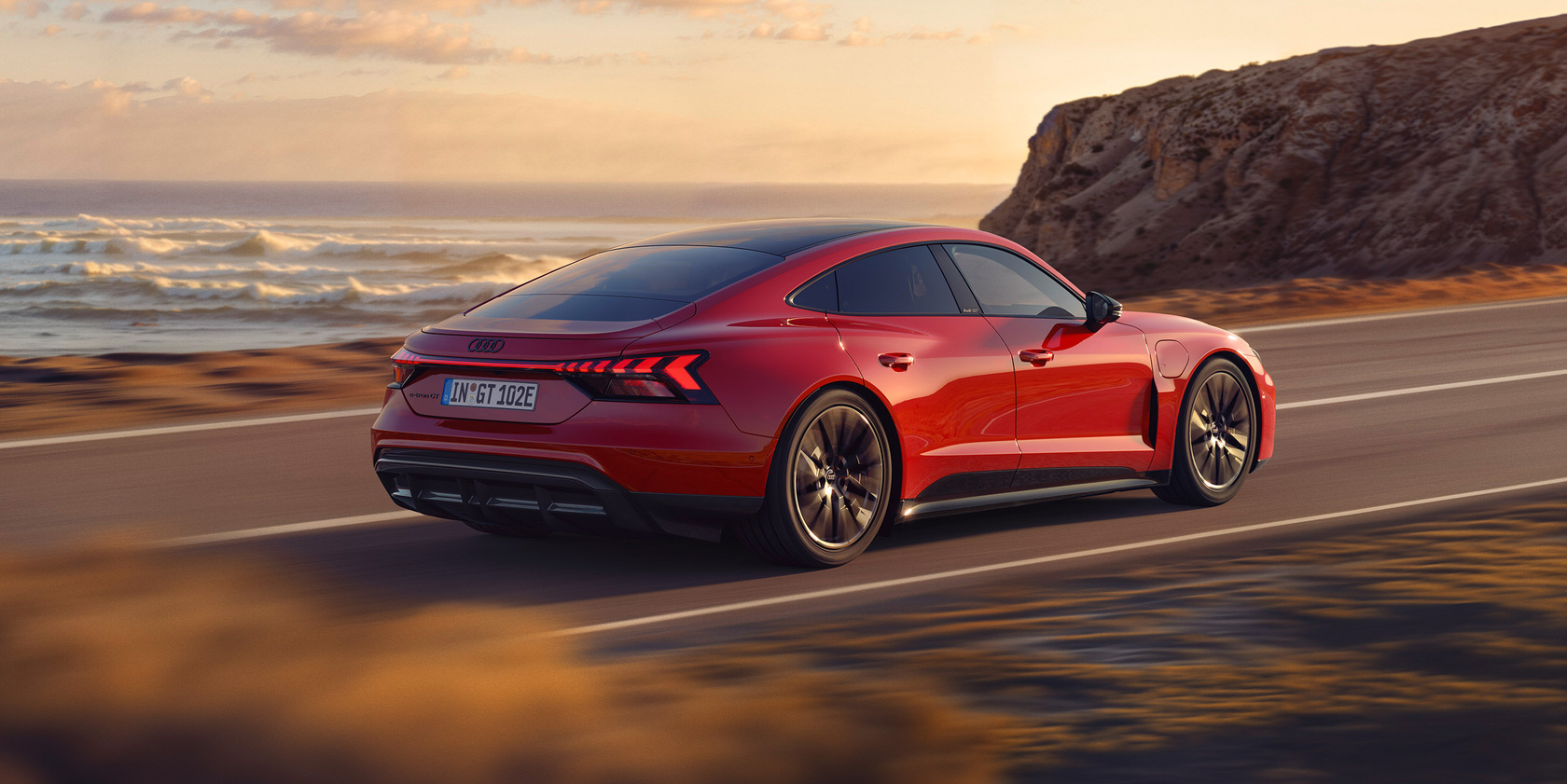 Ein roter Audi e-tron GT fahrend auf einer Straße die an einer Küste liegt.