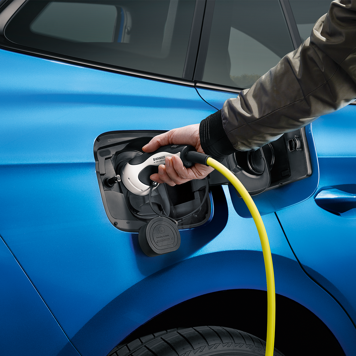 Elektroauto wird geladen – Hand steckt gelbes Ladekabel in blauen E-Auto-Ladeanschluss