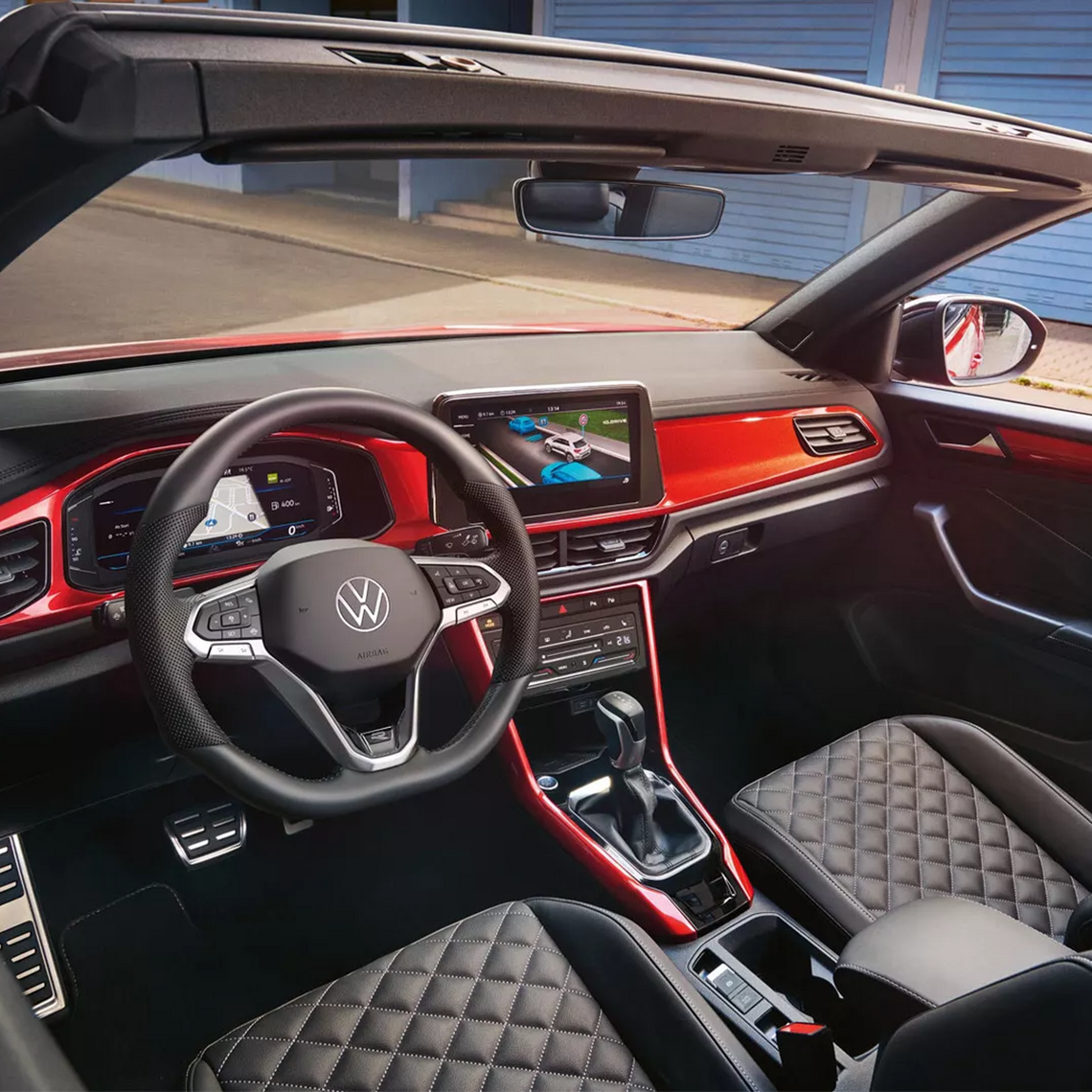 Innenraum eines VW T-Roc Cabriolet mit offenem Verdeck, sportlichem Multifunktionslenkrad, Infotainment-Anzeige und roter Innenverkleidung