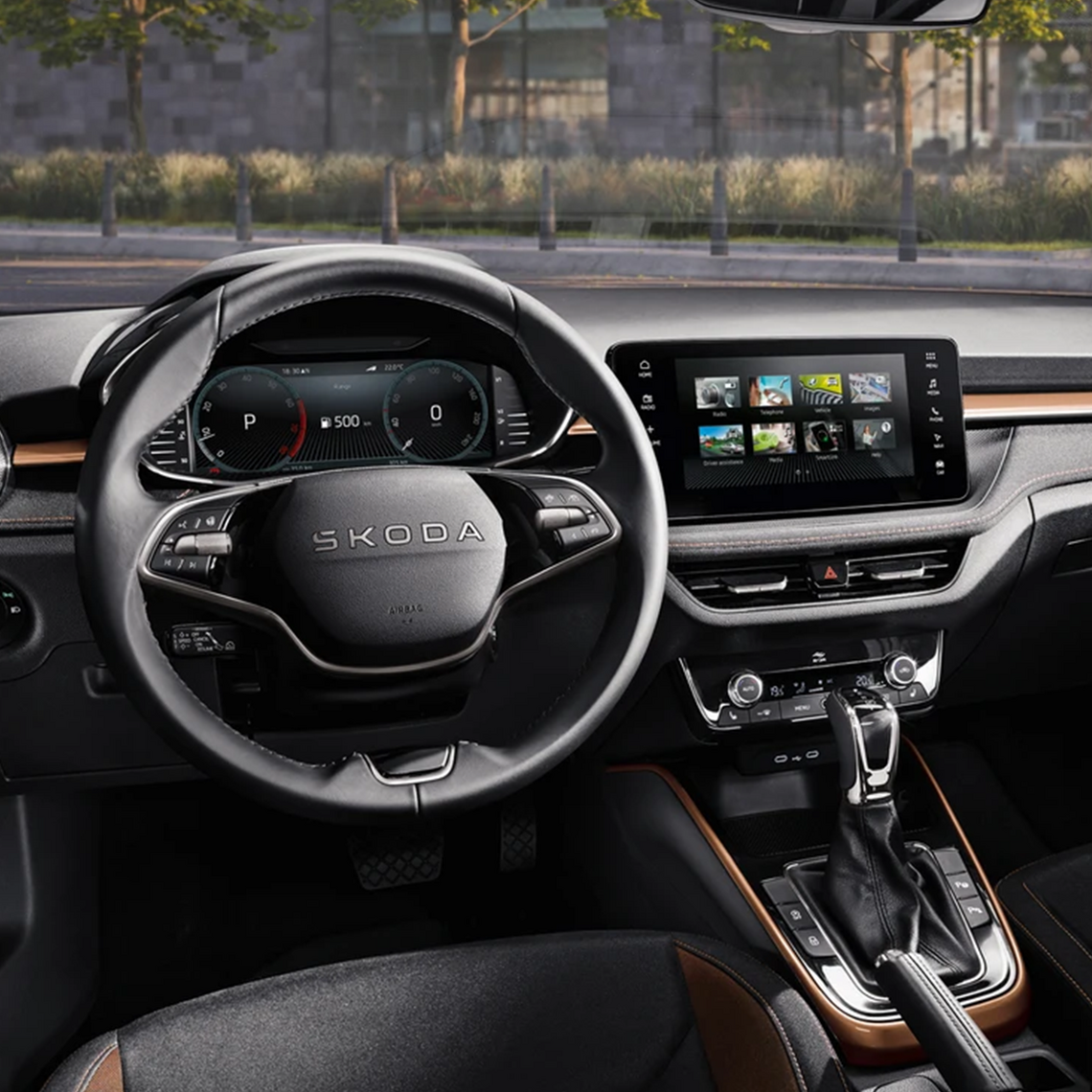 Interieur eines Škoda mit Touchdisplay + Infotainmentsystem, Multifunktionslenkrad und braunen Applikationen an Mittelkonsole, Sitzen und Armaturenbrett.