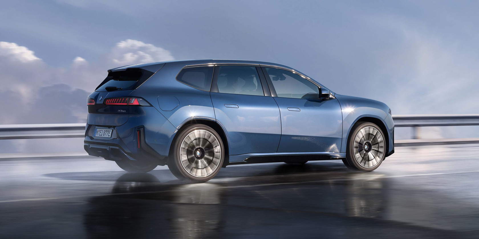 Blauer BMW iX3 fährt dynamisch auf nasser Straße, Seitenansicht mit sportlichem SUV-Design und Leichtmetallfelgen