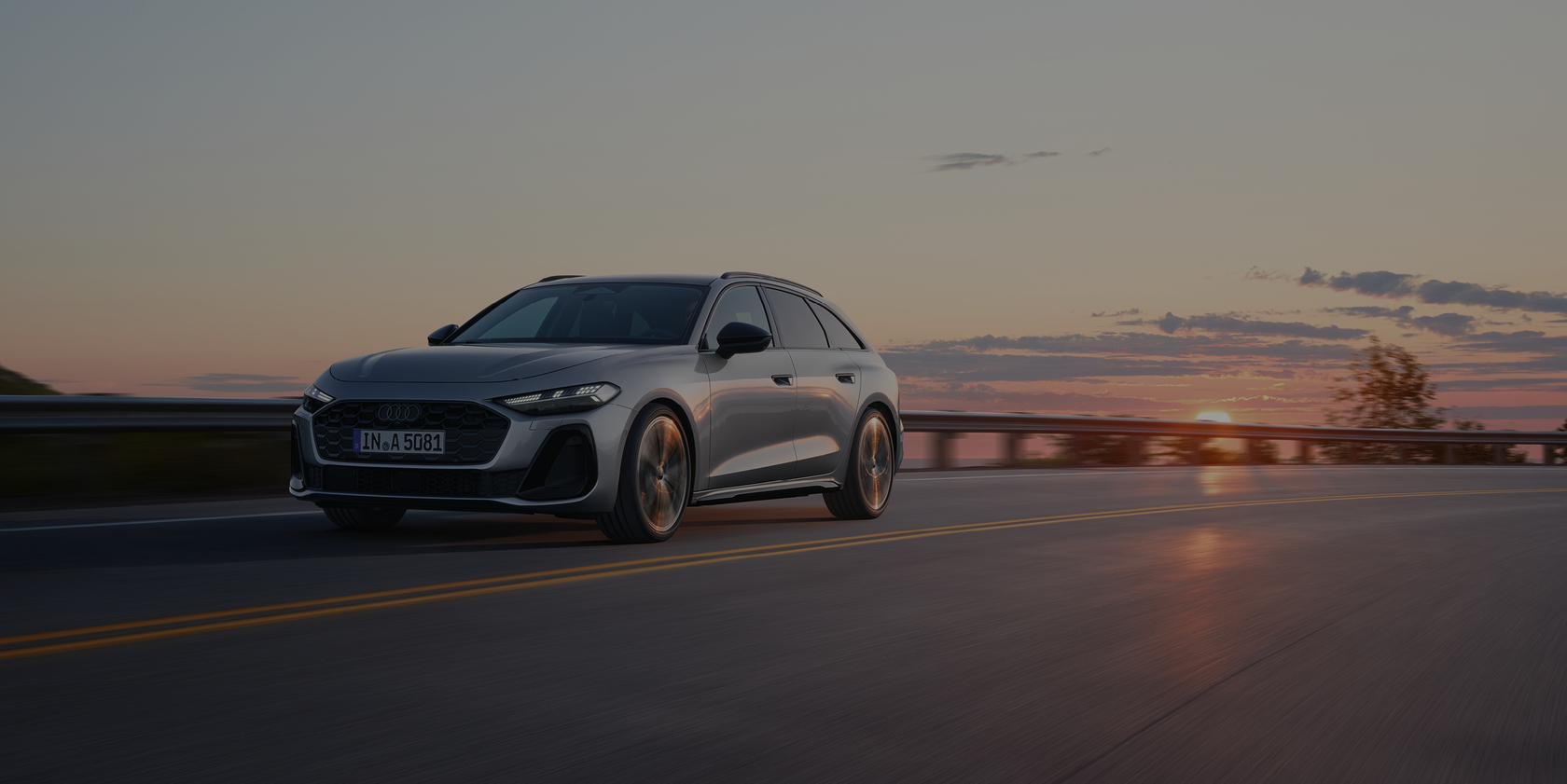 Audi A6 in grau fahrend auf einer Straße; im Hintergrund orangener Himmel bei Sonnenuntergang
