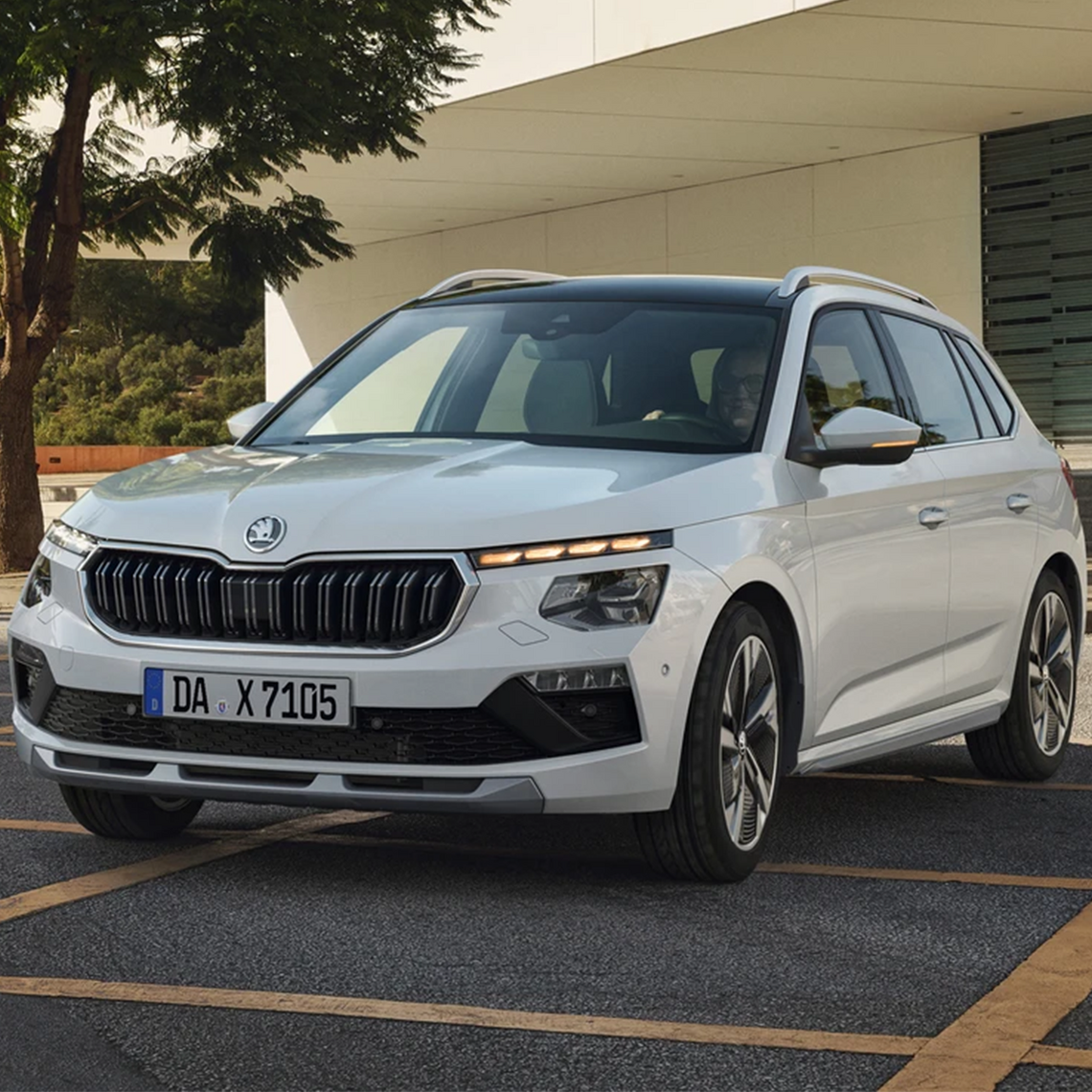 Weißer Škoda Kamiq steht auf einem Parkplatz vor modernem Gebäude.
