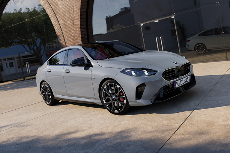 BMW 2er Gran Coupé in Grau parkt vor einer modernen Glasfassade mit Backsteinbogen.