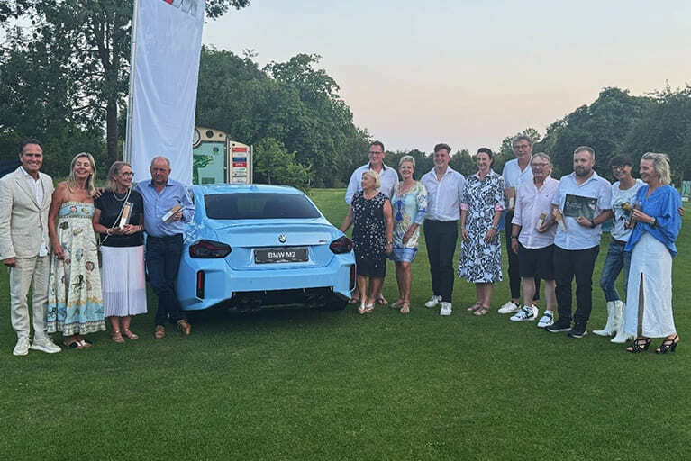 BMW Golf Cup 2025 - Die Geschäftsführer Frau und Herr Elsässer mit den Preisträgern des Golf Cups. In der Mitte ein hellblauer BMW M5