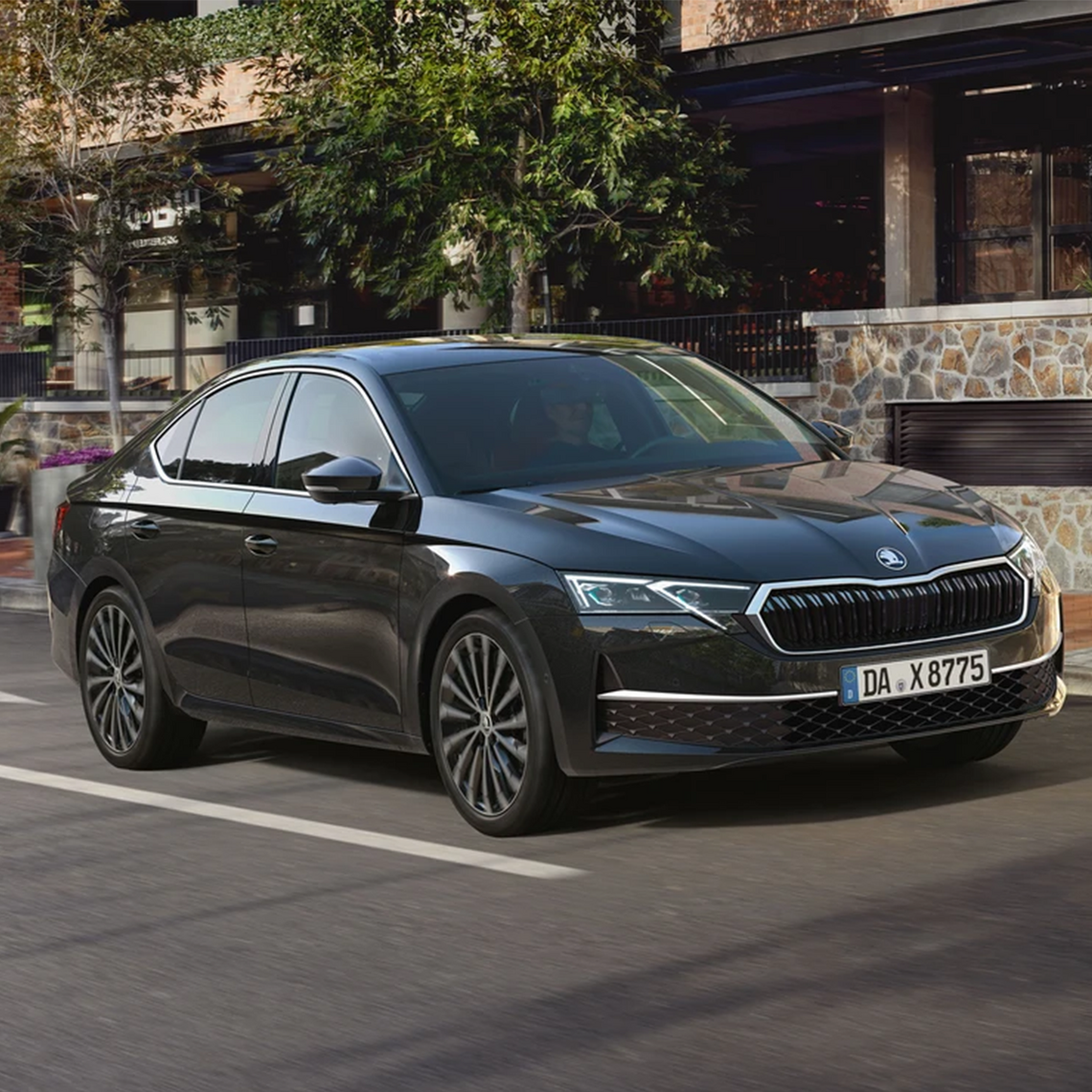Schwarze Škoda Octavia Limousine fährt auf der Straße an einer modernen Steinfassade vorbei.