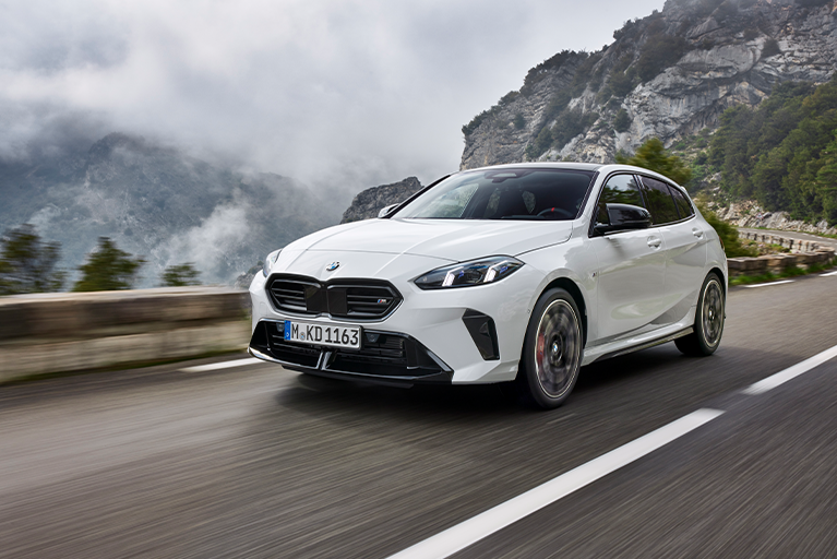 Weißer BMW 1er fährt auf einer Straße entlang in einer Berglandschaft.