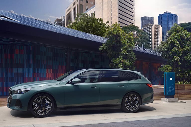 Grüner BMW i5 Touring in Seitenansicht; städtische Umgebung mit Hochhaus im Hintergrund