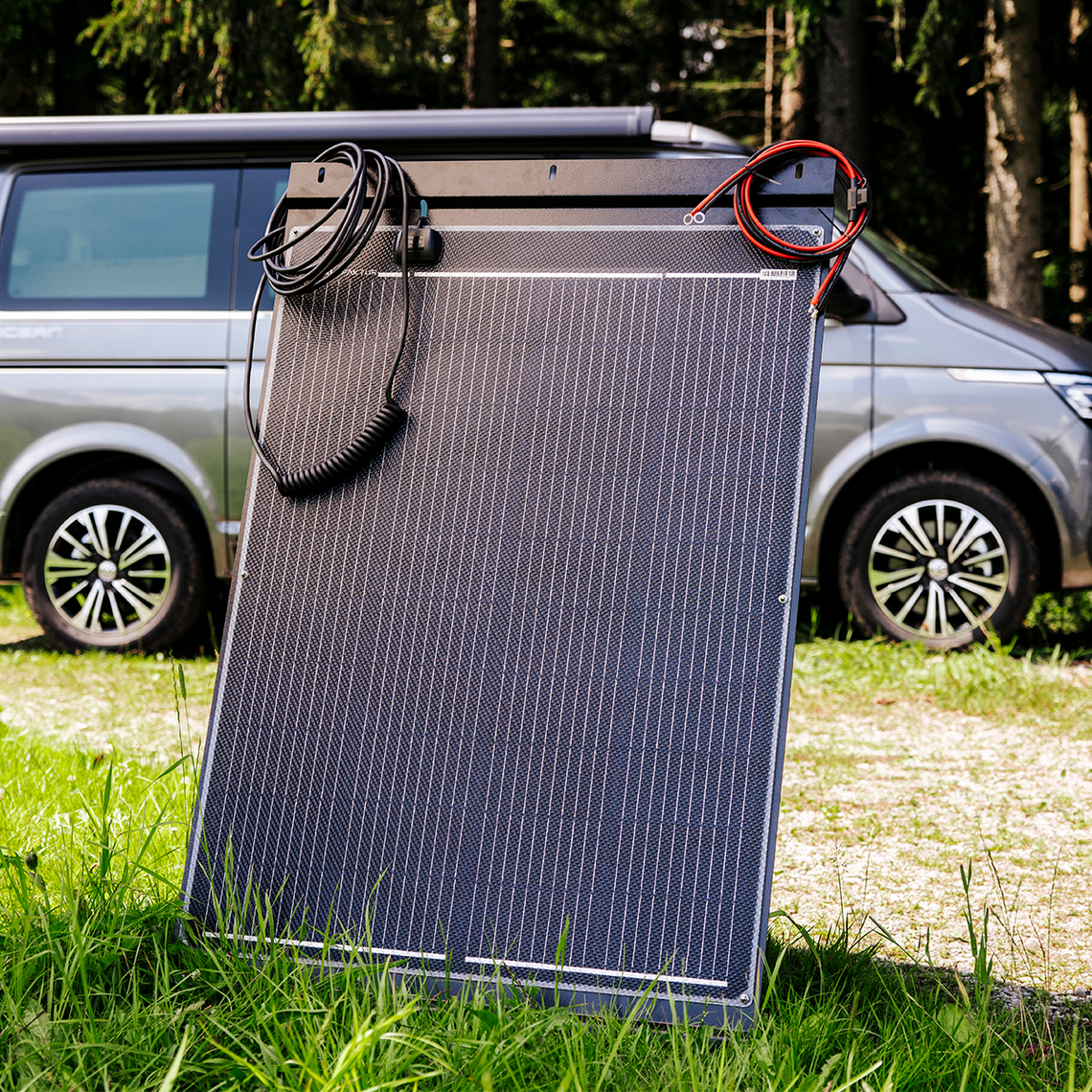 Tragbares Solarmodul mit Kabeln von CALIFAKTUR. Im Hintergrund ein grauer VW California Ocean.