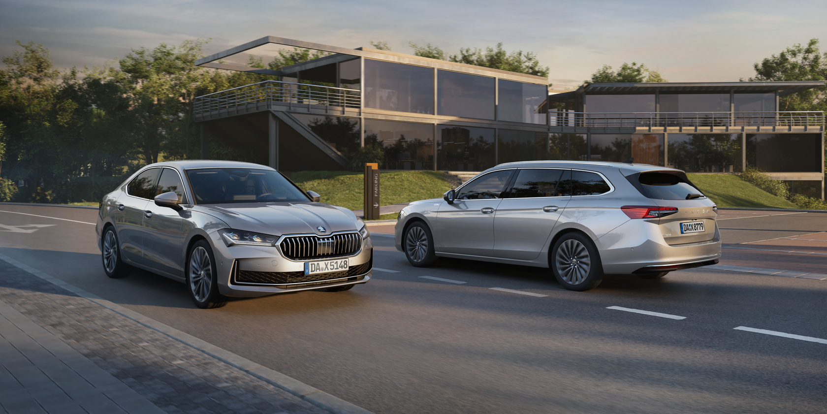 Zwei silberfarbene Škoda Superb-Modelle fahren auf einer Straße in entgegengesetzte Richtungen. Die Škoda Superb Limousine in Frontansicht und der Kombi in Seitenansicht. Im Hintergrund ein modernes Bürogebäude mit Glasfassade