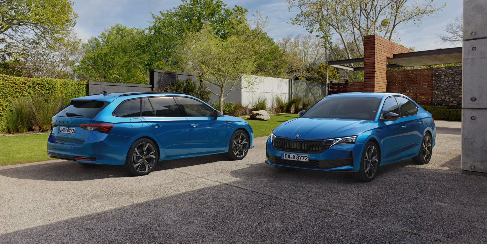 Zwei blaue Škoda Octavia Modelle: links eine Limousine, rechts ein Kombi, stehen in entgegengesetzter Richtung in einer Einfahrt vor einem modernen Gebäude und einer Rasenfläche mit Bäumen im Hintergrund