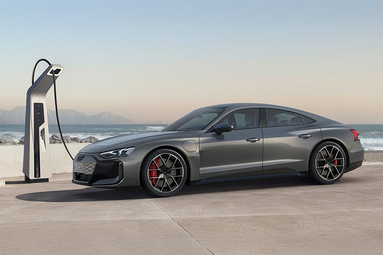 Ein grauer Audi RS e-tron GT lädt an einer E-Ladesäule vor maritimer Kulisse mit Bergen und Meer im Hintergrund.