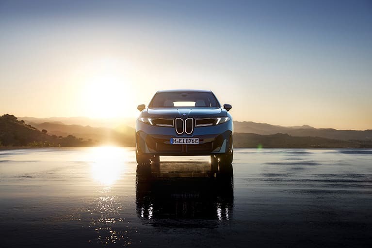 Der neue BMW iX3 in dunkelblau, Frontansicht im Hintergrund ein Sonnenuntergang