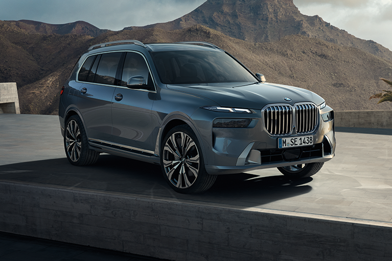 BMW X7 in Grau-Blau steht vor einer beeindruckenden Gebirgslandschaft.