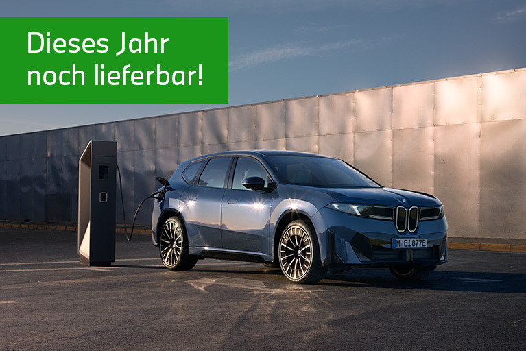 Blauer BMW iX3 steht angeschlossen an einer Ladesäule vor einem modernen Gebäude. Oben links steht auf grünem Hintergrund der Hinweis ‚Dieses Jahr noch lieferbar!