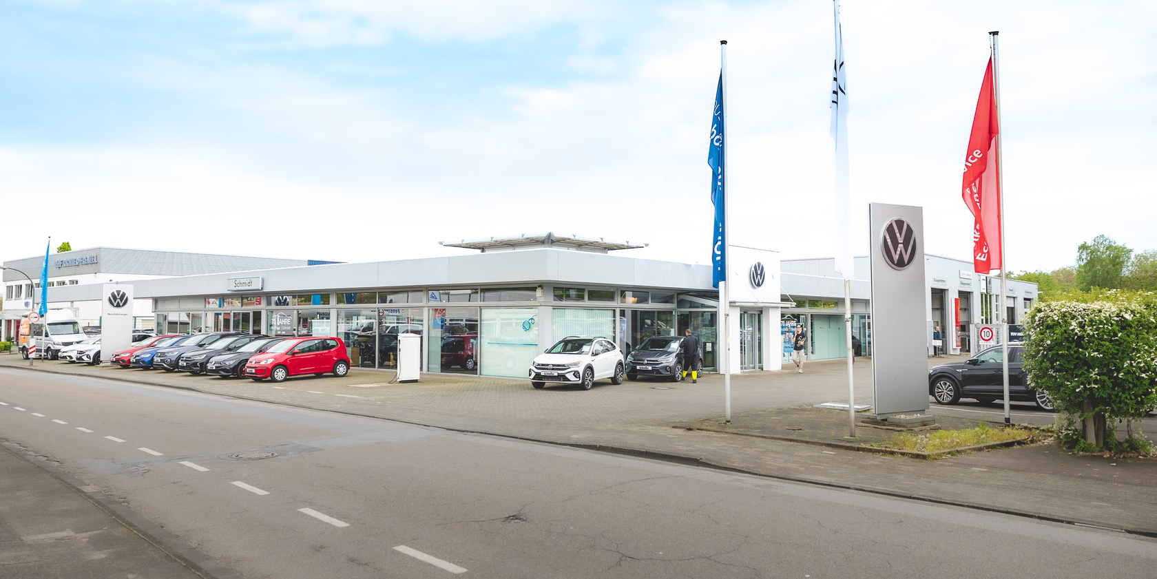 Außenansicht des Autohauses Schmidt am Standort Recklinghausen. Vor dem Glasgebäude stehen einige unterschiedliche VW Modelle in verschiedenen Farben.