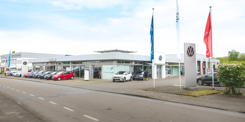 Außenansicht des Autohauses Schmidt am Standort Recklinghausen. Vor dem Glasgebäude stehen einige unterschiedliche VW Modelle in verschiedenen Farben.