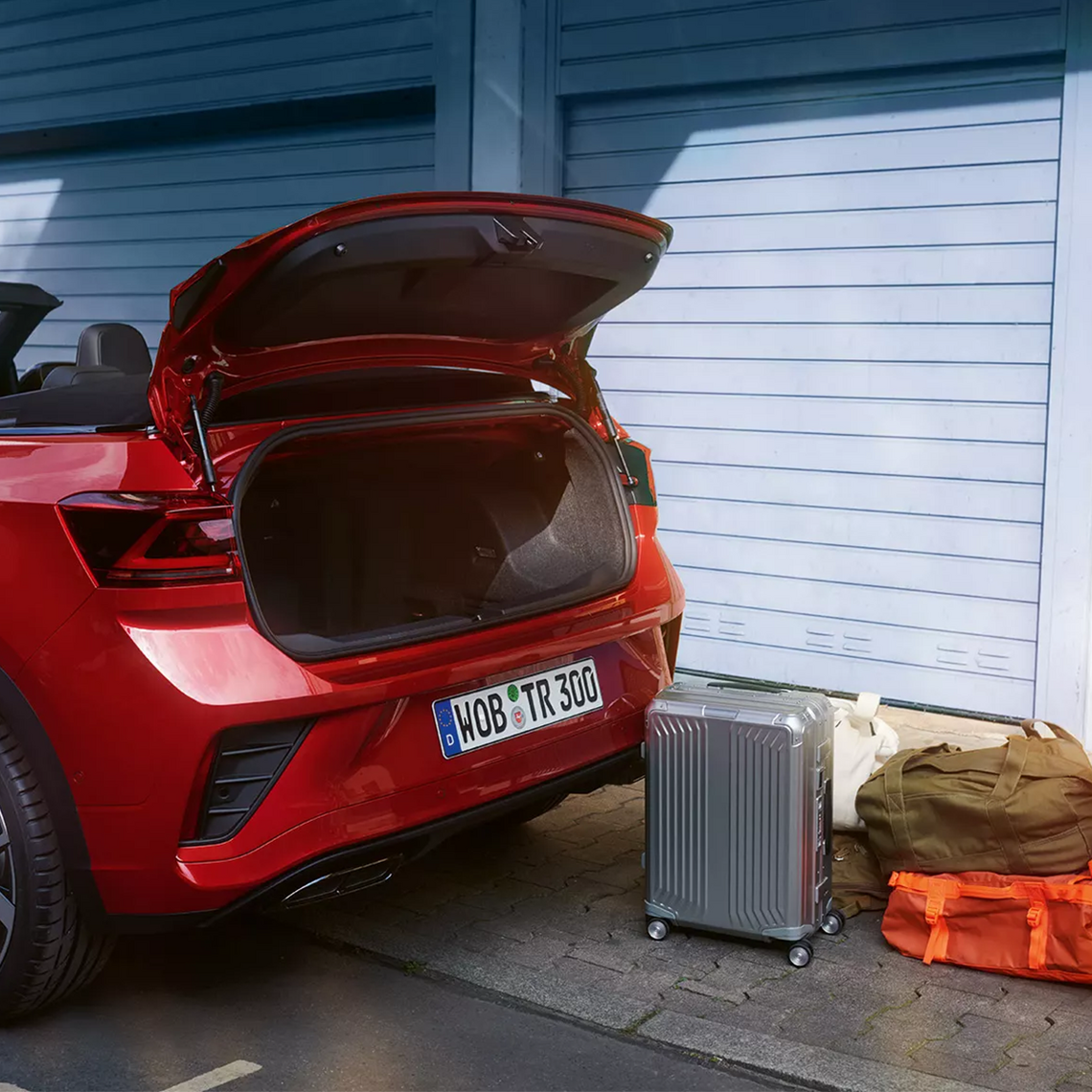 Offene Heckklappe eines roten VW T-Roc Cabriolet mit Reisekoffern und Taschen daneben.