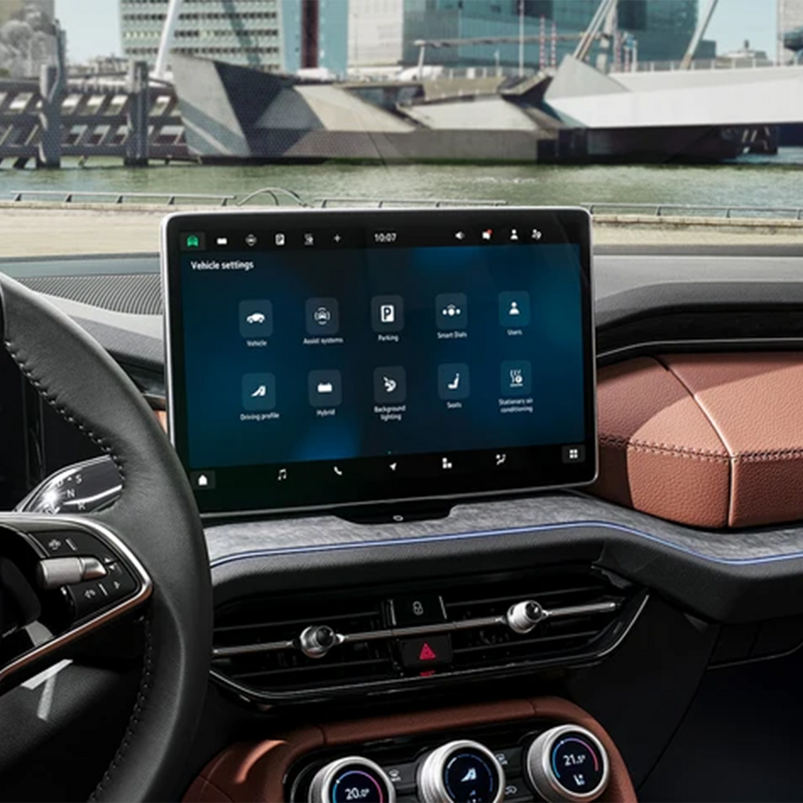 Großes Touchdisplay im Škoda Kodiaq zeigt Fahrzeugmenü, modernes Cockpit mit Ledersitzen, Blick auf einen Hafen durch die Frontscheibe