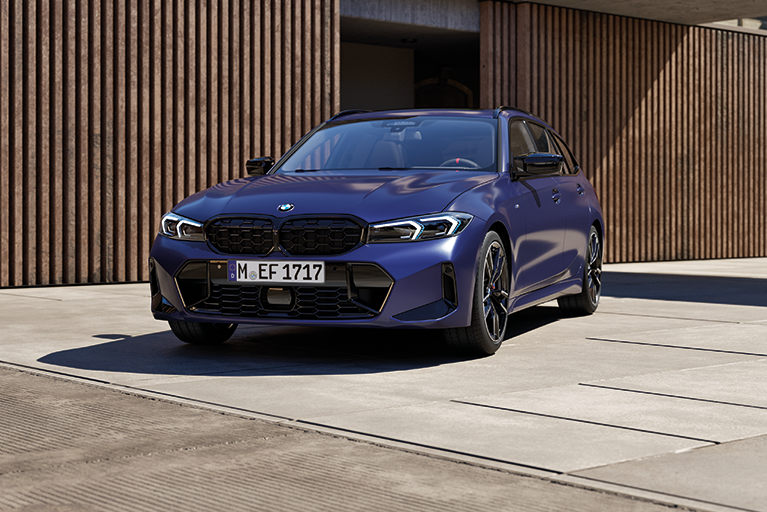 BMW 3er Touring in kräftigem Blau vor einer modernen Holzfassade.